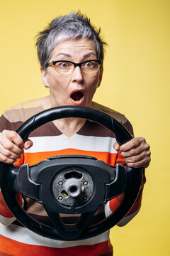 Mature woman expressing shock and fear, holding a car steering wheel, symbolizing danger, accident, or driving stress