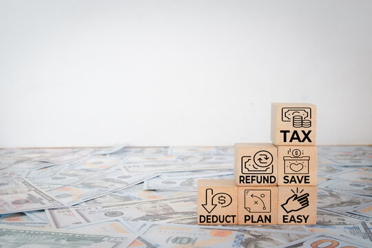Tax planning and financial return concept. Wooden blocks with tax, refund, save, and deduct text on US dollar banknotes background. Wealth management, economy and accounting with copy space.