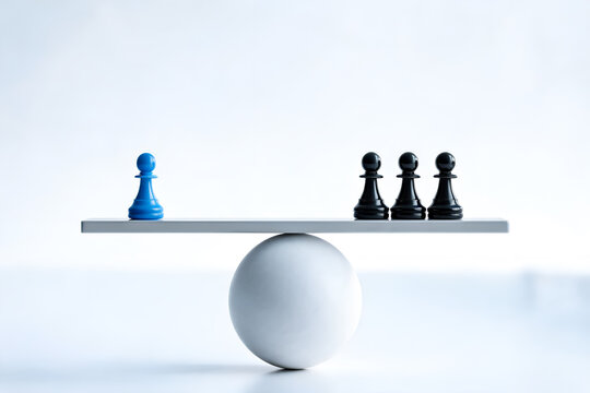 Chess pawns on balance scale one blue pawn opposite three black pawns concept of inequality power strategy or unequal opposition