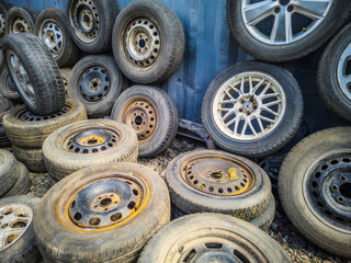 Pile of Used Car Tires and Wheels Against Metal Wall © lucky pics