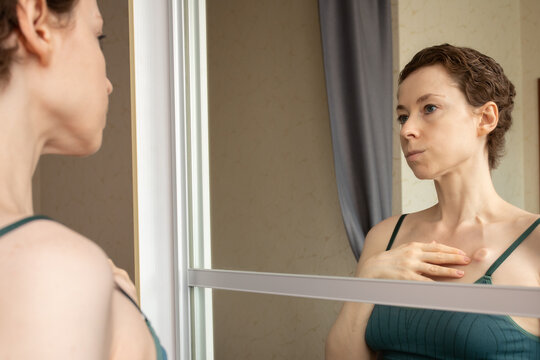 reflective mirror portrait of a woman touching the area around her implanted port, illustrating calm monitoring, body awareness and real patient experience after treatment