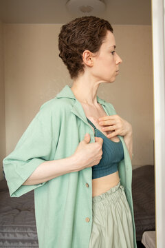 close side portrait of a woman with a visible chest port gently adjusting clothing, representing real patient experience, oncology care and daily life after cancer treatment
