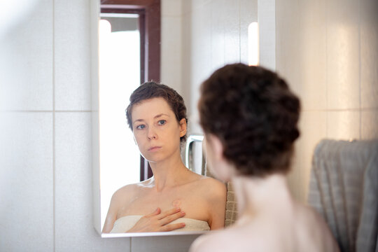 post shower bathroom scene of a woman gently covering her implanted port area, showing tenderness, body awareness and realistic self care during oncology recovery