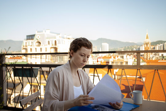 woman after cancer treatment reads healthcare papers from a blue folder on a terrace, representing patient advocacy, medical planning, recovery and independent living