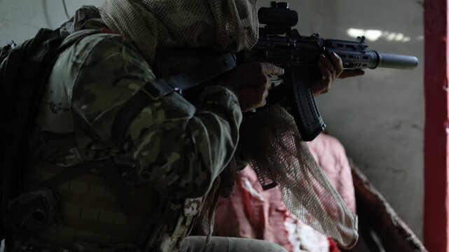 Witness the art of patience as a soldier prepares in an abandoned barn. With meticulous care, he raises his automatic rifle, demonstrating the calm before the storm of engagement.