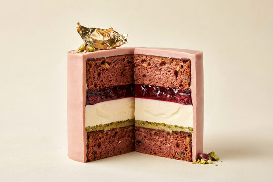 Cut slice of layered chocolate and vanilla cake with berry jam filling, festive gold decoration and crumbs on beige background for dessert advertising