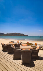 Beachfront cafe in Quy Nhon, Vietnam, with tables, chairs and sunshades overlooking the sea, gentle waves and fishing boats in the background on a sunny day. © Olga Khoroshunova