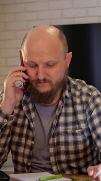 Man at desk verifies appointment details. Individual checks calendar and notes with focused expression. Person in plaid shirt assesses schedule and notes at tidy workspace during daytime