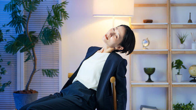 室内でぐったりする女性ビジネスパーソン。疲労、疲れ、残業、ストレス、放心、落ち込む、過労、仕事、夜