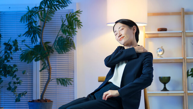 暗い部屋でリラックスする女性ビジネスパーソン。ストレス、疲れ、肩こり、休憩、残業、帰宅、夜、息抜き