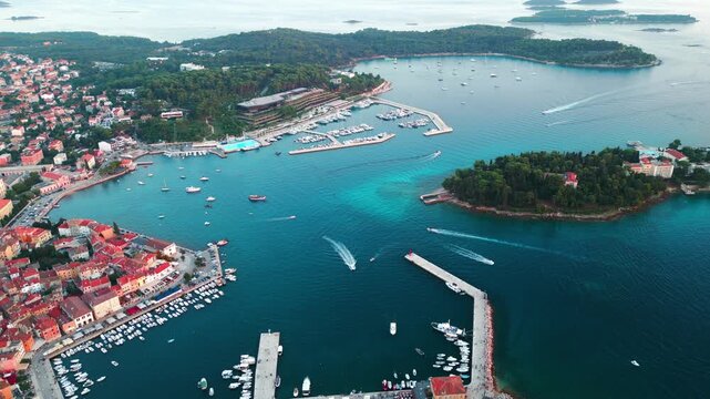 drone footage above Rovinj marina, harbor entrance and surrounding Adriatic islands with boats crossing crystal-clear water. Summer tourism and luxury sailing concept