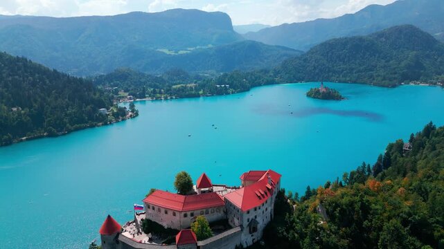 Cinematic drone flight above the medieval Bled Castle with panoramic views of turquoise Lake Bled, the iconic island church, forested hills and the Julian Alps in Slovenia