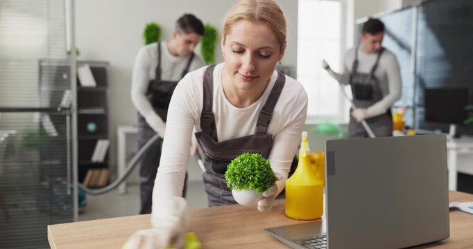 Cleaners team housekeeper dusting office workspace hygiene. Janitors mop and vacuum while the housekeeper wipes a desk during cleaning to ensure sanitation. Clean office theme active now.