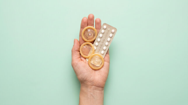 Hand holding contraceptive pills and condoms on green background  