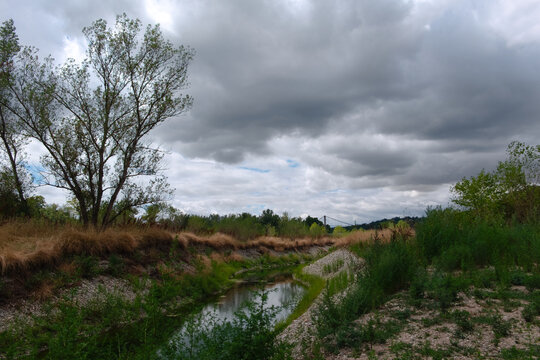 Petit cours d'eau en cours d'ass&egrave;chement bord&eacute; de v&eacute;g&eacute;tation sauvage sous un ciel d'orage matinal (L&ocirc;ne vers Lyon sur le Rh&ocirc;ne).