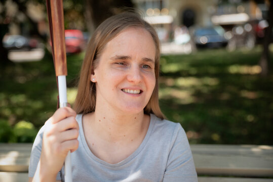 Visually impaired young woman with white cane relaxing in a city park on a summer day
