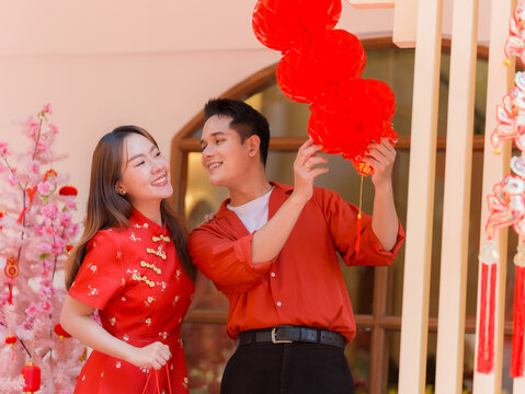 Asian couple wearing red traditional clothing giving gift bag during Chinese New Year celebration, romantic young couple smiling together in festive atmosphere