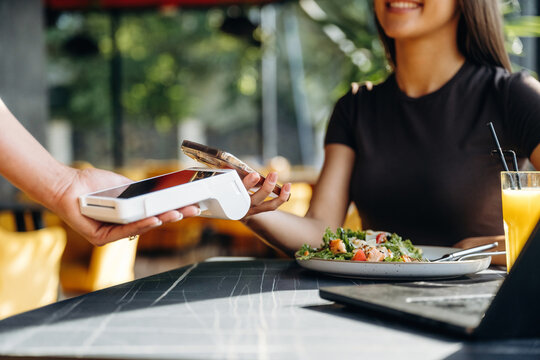 Young woman at restaurant table using mobile payment with card reader while enjoying a fresh salad and orange juice in a modern dining environment