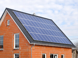 Fototapeta premium Eine Photovoltaikanlage auf dem Hausdach von einem Neubau erzeugt grünen Strom