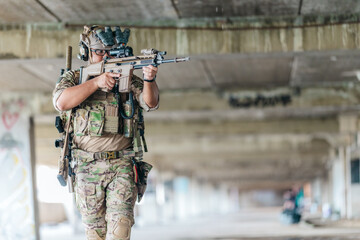 Fototapeta premium Military tactical operator holds rifle while clearing abandoned concrete building interior