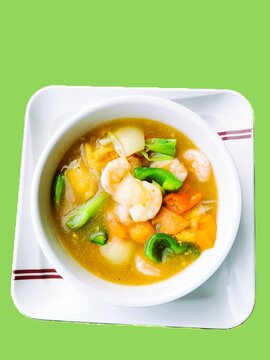 Top view of delicious Asian shrimp vegetable soup in a white bowl on green background