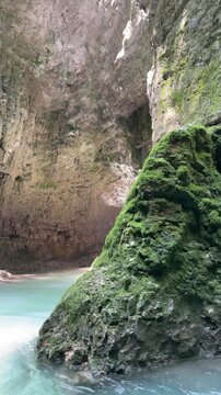turquoise water flows through a dramatic moss-covered limestone canyon, with rugged cave walls, gentle river movement and soft light creating an untouched wilderness atmosphere
