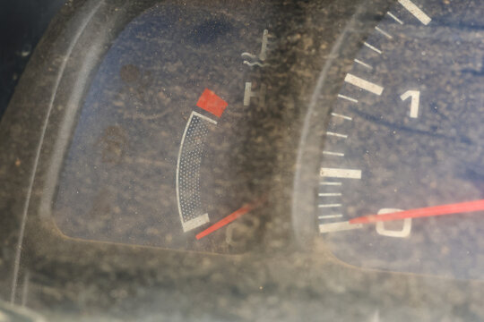 Dusty car instrument cluster with low fuel indicator and tachometer needle visible, gritty texture and worn dashboard conveying neglect and mood