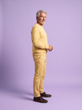 Selbstbewusster grauhaariger Mann in gelber Kleidung blickt in Untersicht &uuml;ber die Schulter vor fliederfarbenem Hintergrund