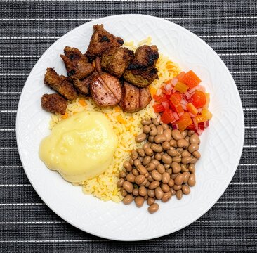 A delicious plate of food featuring grilled meat, rice, beans, mashed potatoes, and pico de gallo, perfect for a hearty meal.