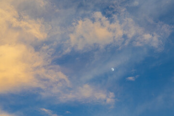 Fototapeta premium Golden cloud and blue sky with partial moon visible at dusk, soft warm light and airy texture creating calm atmospheric scene
