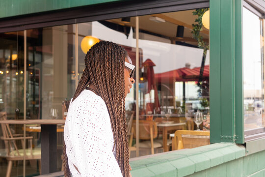 Young woman in profile, with an Afro-braided hairstyle, leaning against a restaurant window.