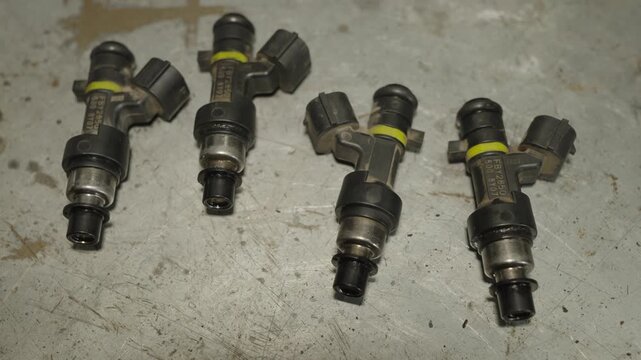 Four car fuel injectors lying on a scratched metallic workbench surface.