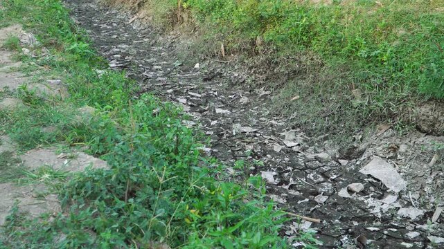 Panning shot of completely dried up irrigation canal in rural farmland showing severe drought and El Nino impact in Indonesia.