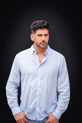 Fototapeta premium Handsome young man in a light blue button-down shirt portrait against isolated black background