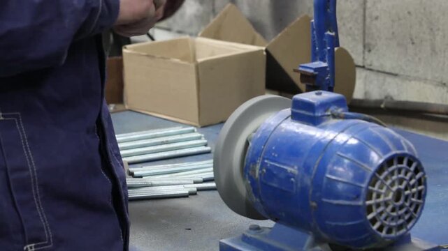 a worker is sharpening a threaded metal rod on a grinder