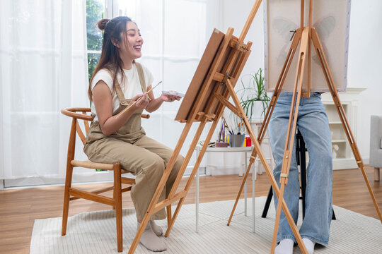 Two young Asian women painting a colorful landscape on canvas together