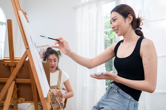 Two young Asian women painting a colorful landscape on canvas together