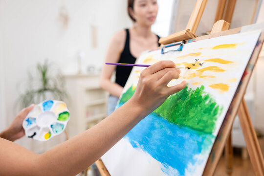 Close up of a young Asian woman painting birds in the sky for a landscape on canvas