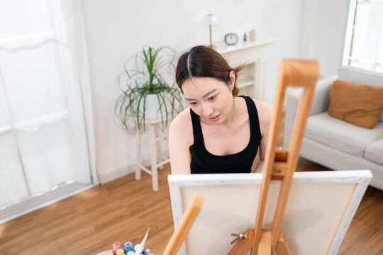 Young Asian woman painting on canvas in a bright home art studio during the weekend