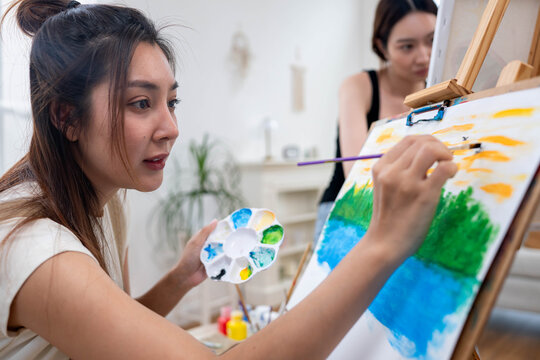 Close up of a young Asian woman painting birds in the sky for a landscape on canvas