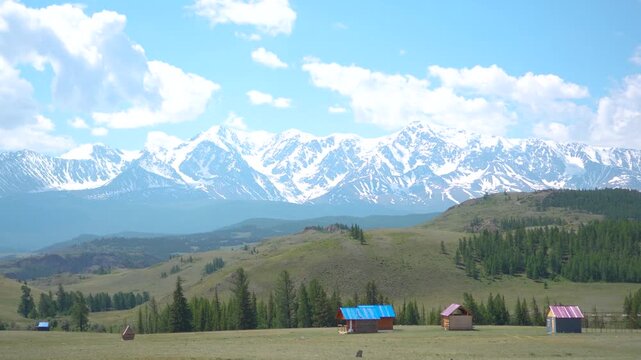 Inspiring panoramic footage moving from right to left revealing an eco friendly mountain resort with small tourist cabins under a majestic snow-covered ridge in the Kurai Steppe.