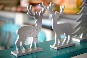 Two silver wooden reindeer Christmas decoration figures stand on a turquoise shelf, creating a festive winter interior ornament display with antlers, rustic texture and softly blurred background. © Yulia Mihaylova