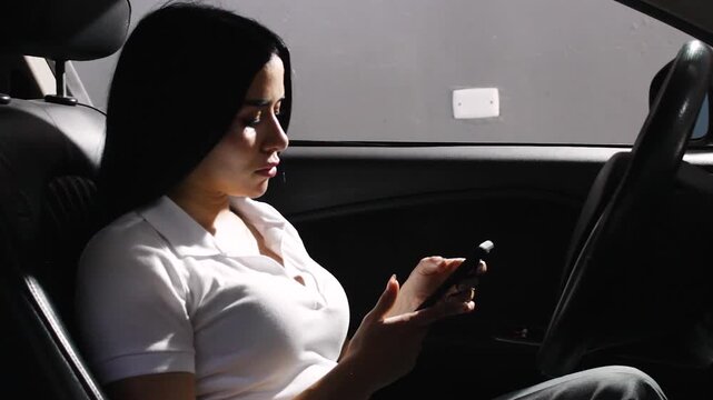 A beautiful young Colombian woman is chatting on her smartphone inside a car in Neiva, Huila, Colombia. Concept of businesswoman and technology
