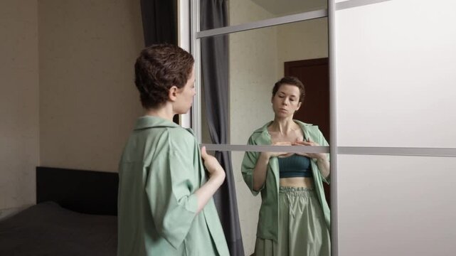 woman carefully moves a shoulder strap away from a sensitive chest port while dressing by the mirror, showing discomfort, self care and oncology lifestyle at home
