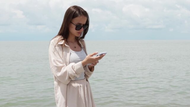 teenage tourist uses a smartphone on a sunny pebble beach by the sea, combining travel planning, mobile connection, weather awareness, heat safety and hydration reminders