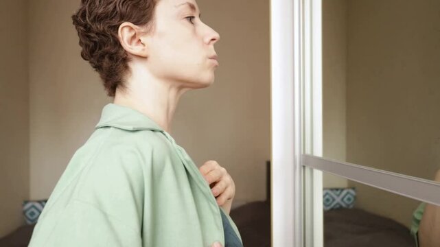 woman carefully pulls fabric away from a sensitive port area while looking in the mirror, showing clothing adaptation, patient comfort and life with an implanted port