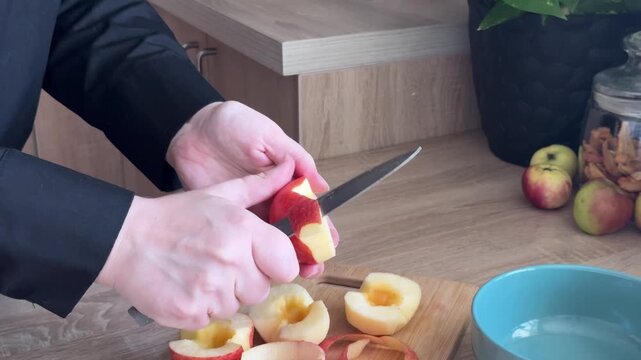 Peeling a Fresh Red Apple with a Knife for Homemade Apple Strudel, Preparing Fruit for Baking on Wooden Cutting Board in Home Kitchen