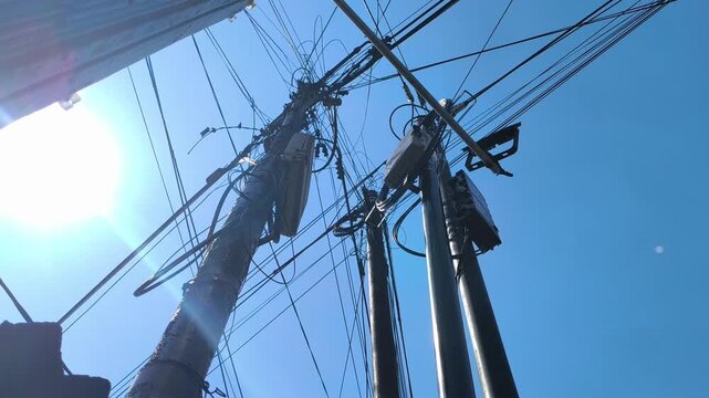 A utility pole supporting overhead power lines and tangled communication cables in an urban setting, illustrating electrical infrastructure, telecommunications networks, and city utility systems.