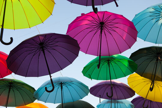Bright umbrellas hang against the open sky, colorful outdoor installation, creative decorative display, festive summer atmosphere.
