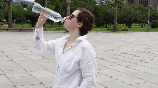 female cancer survivor drinks water beside city greenery, highlighting hydration during hot weather and mindful wellbeing after cancer therapy during a restorative summer walk outdoors